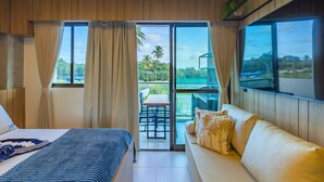 Ein Hotelzimmer mit Bett, Sofa, Esstisch und Blick auf Pool und Palmen.
