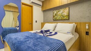 Ein Hotelzimmer mit Bett, Holz-Kopfteil, Wandklimaanlage und einem tropisch gestalteten Bild.
