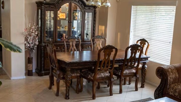 A dining area with a large wooden table and chairs, a decorative mirror, and a chandelier.