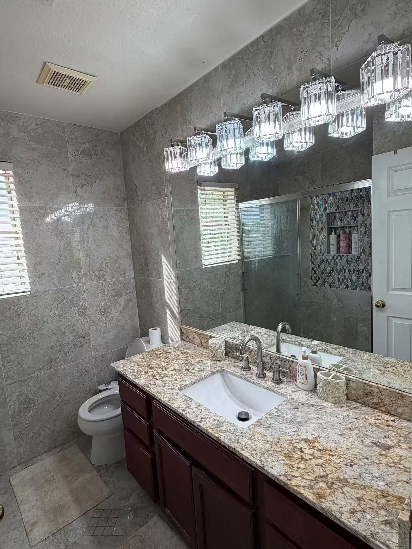 Un baño con encimera de mármol, lavamanos doble, un espejo grande y una lámpara en el techo.