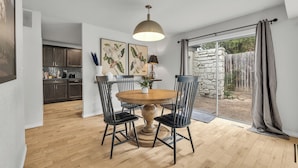 A dining area with a round wooden table, black chairs, a pendant light, and a view of a stone wall and garden through a sliding glass door. - Spacious Hilltop Retreat in Upscale Cul-de-Sac Neighborhood (Tulsa)