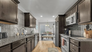 A modern kitchen with dark wood cabinets, granite countertops, stainless steel appliances, and a wooden floor. - Spacious Hilltop Retreat in Upscale Cul-de-Sac Neighborhood (Tulsa)