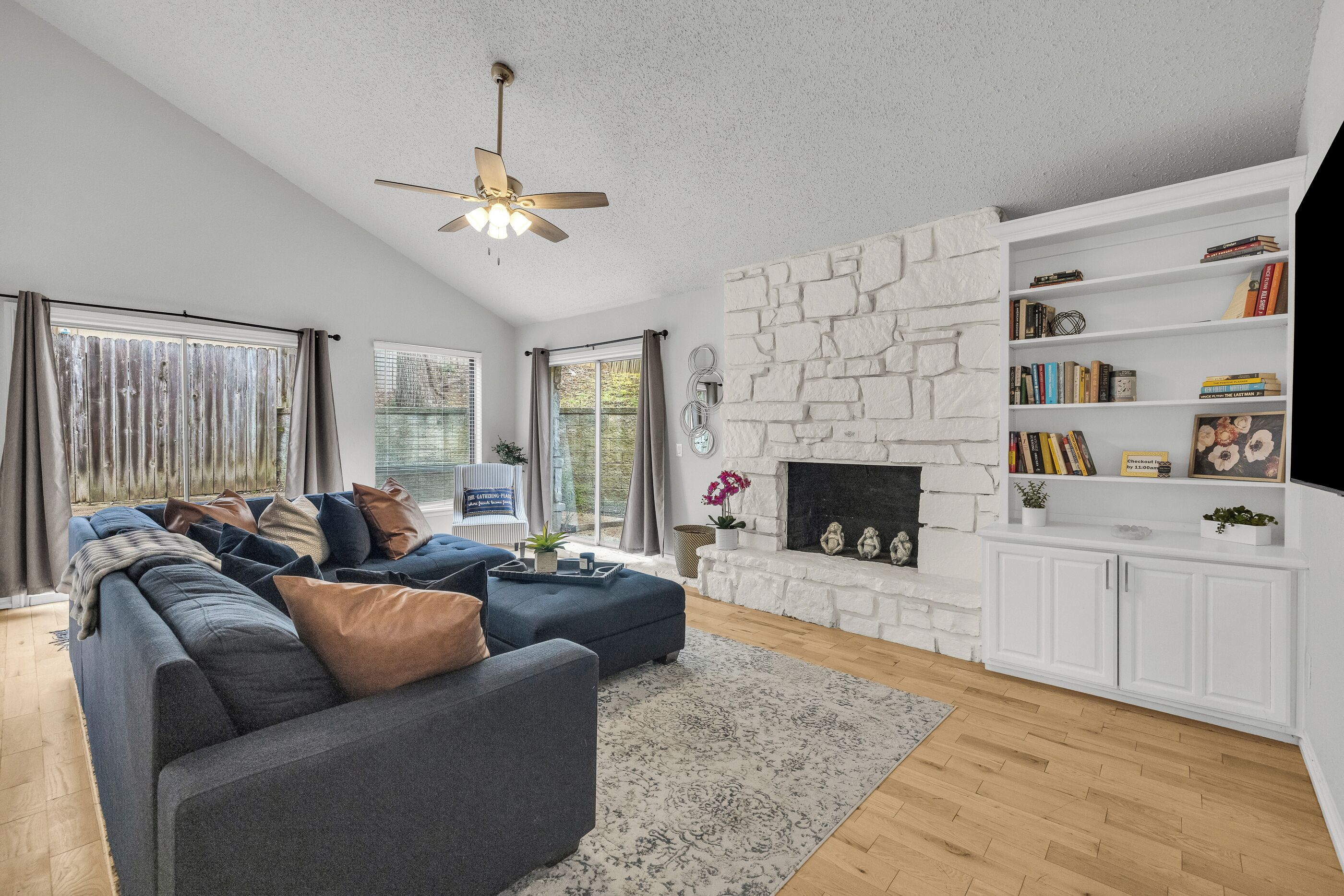 A living room with a sectional sofa, a fireplace, a bookshelf, and a ceiling fan.