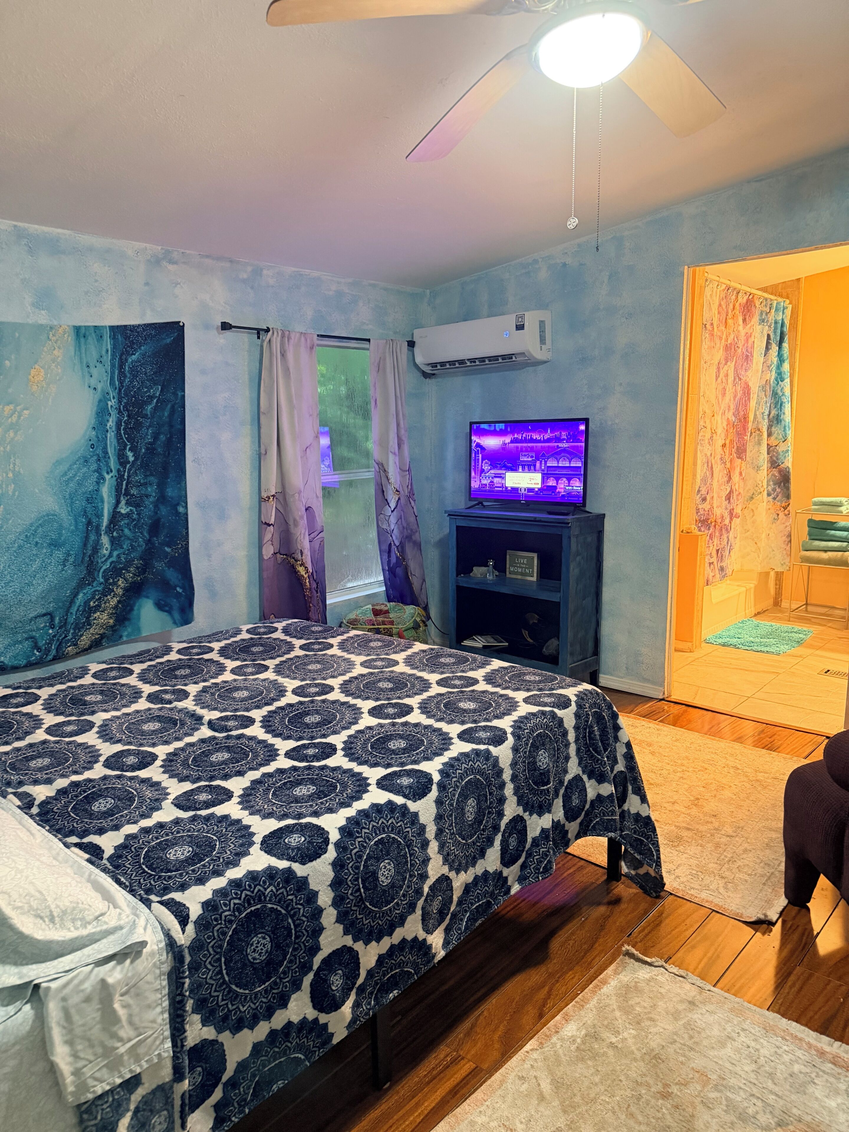 A bedroom with a bed, a TV, an air conditioner, and a window with curtains.