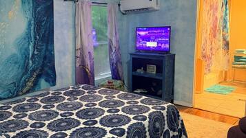 A bedroom with a bed, a TV, an air conditioner, and a window with curtains.