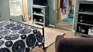 A bedroom with a bed, a TV on a stand, a bookshelf, and a door leading to another room.