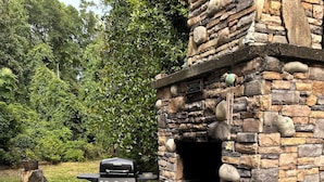 An outdoor patio with a stone fireplace, a grill, and green Adirondack chairs.