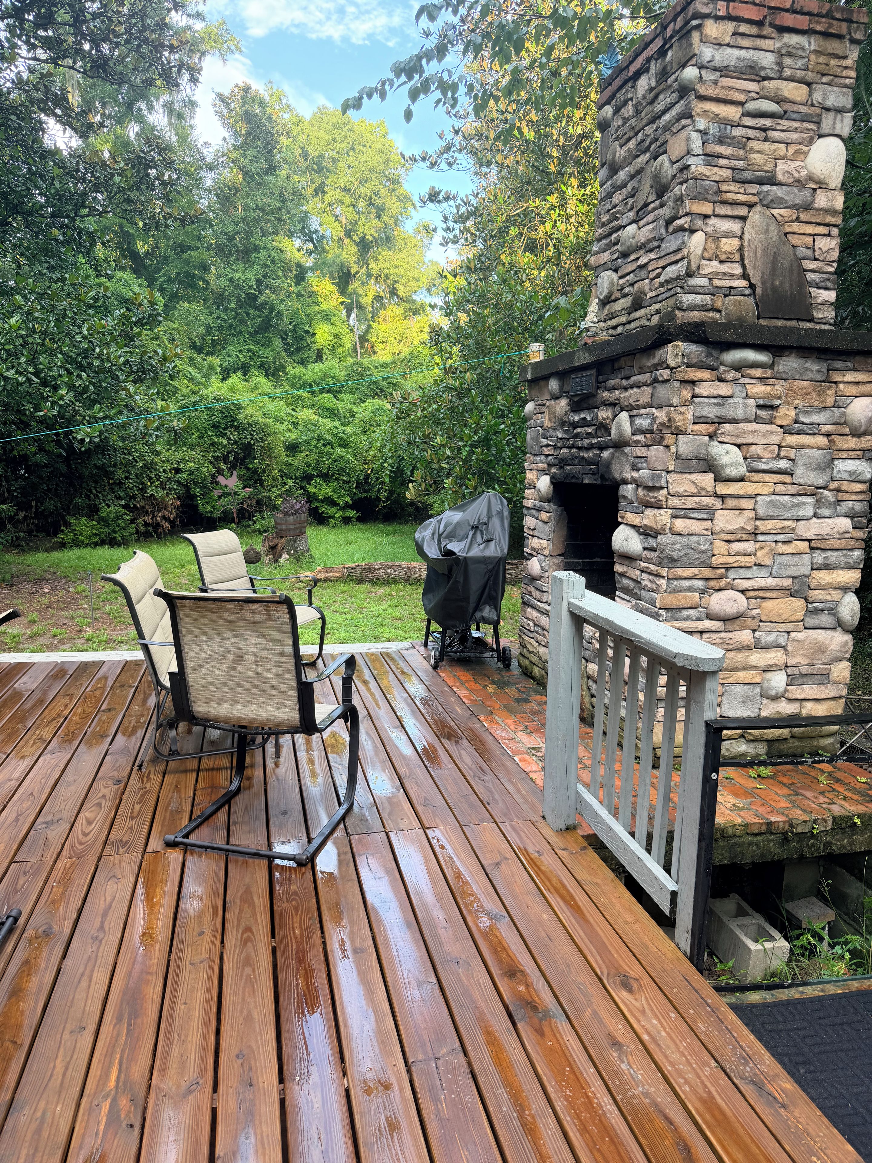 A wooden deck with a stone fireplace, outdoor furniture, and a grill.