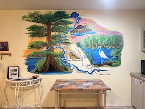 A wall mural with a map-like design, a table, and a framed welcome sign.