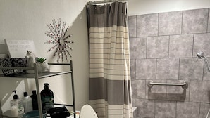 A modern bathroom with a shower, toilet, and a shelf with toiletries.
