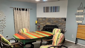 A dining area with a wooden table and four chairs, a stone fireplace, and motivational wall art.
