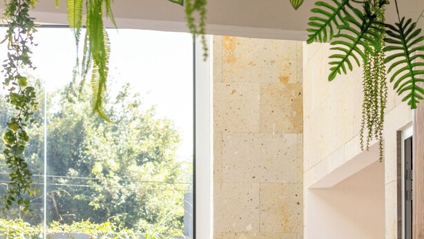 Ein moderner Poolbereich im Innenbereich mit freiem Blick ins Freie, einschließlich einer Backsteinmauer und Grünpflanzen. In der Nähe des Pools befinden sich zwei Holzstühle und ein Blumentopf.