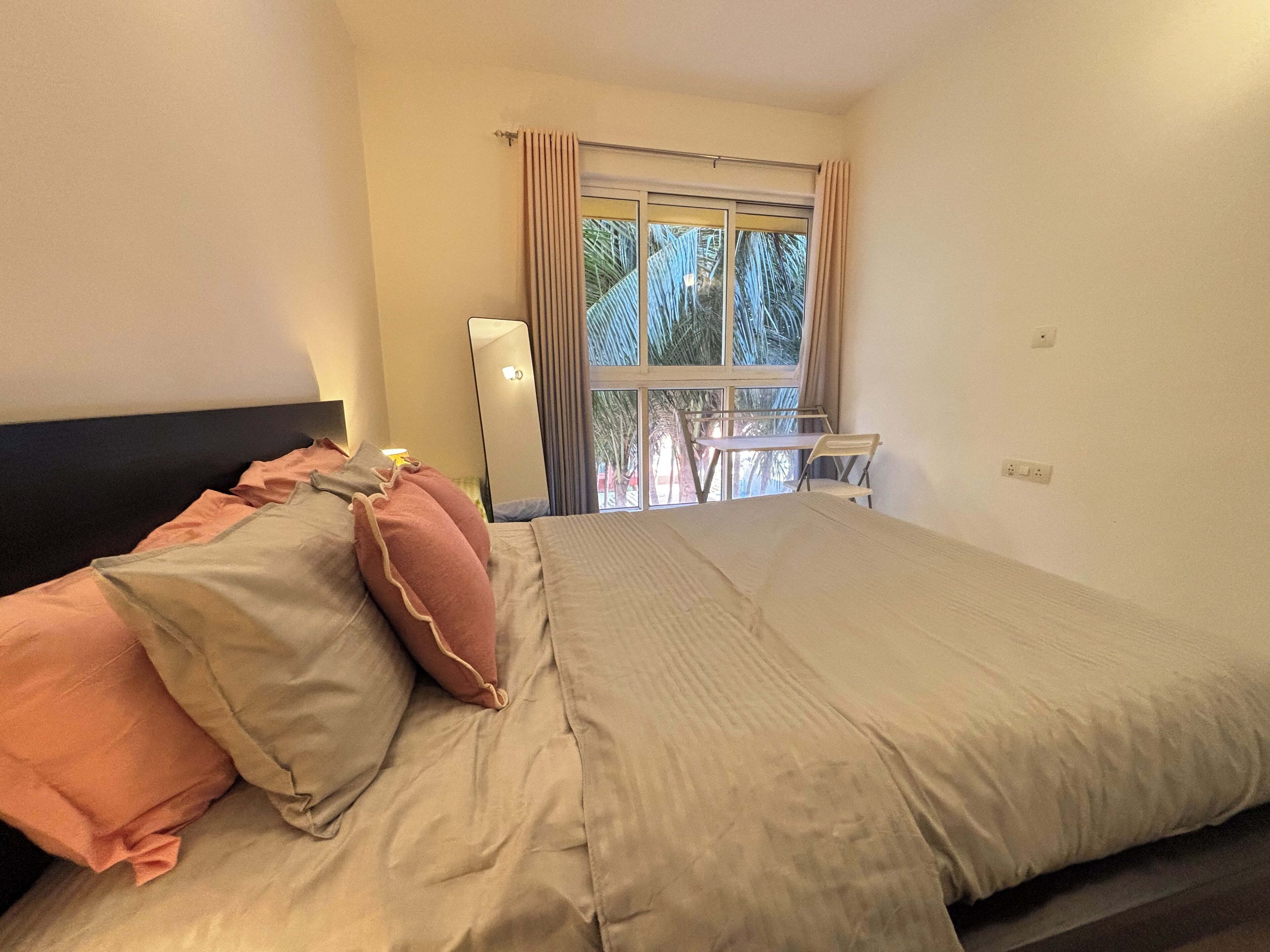 Una cama bien hecha con almohadas, una mesita de noche, una lámpara y una ventana con cortinas.