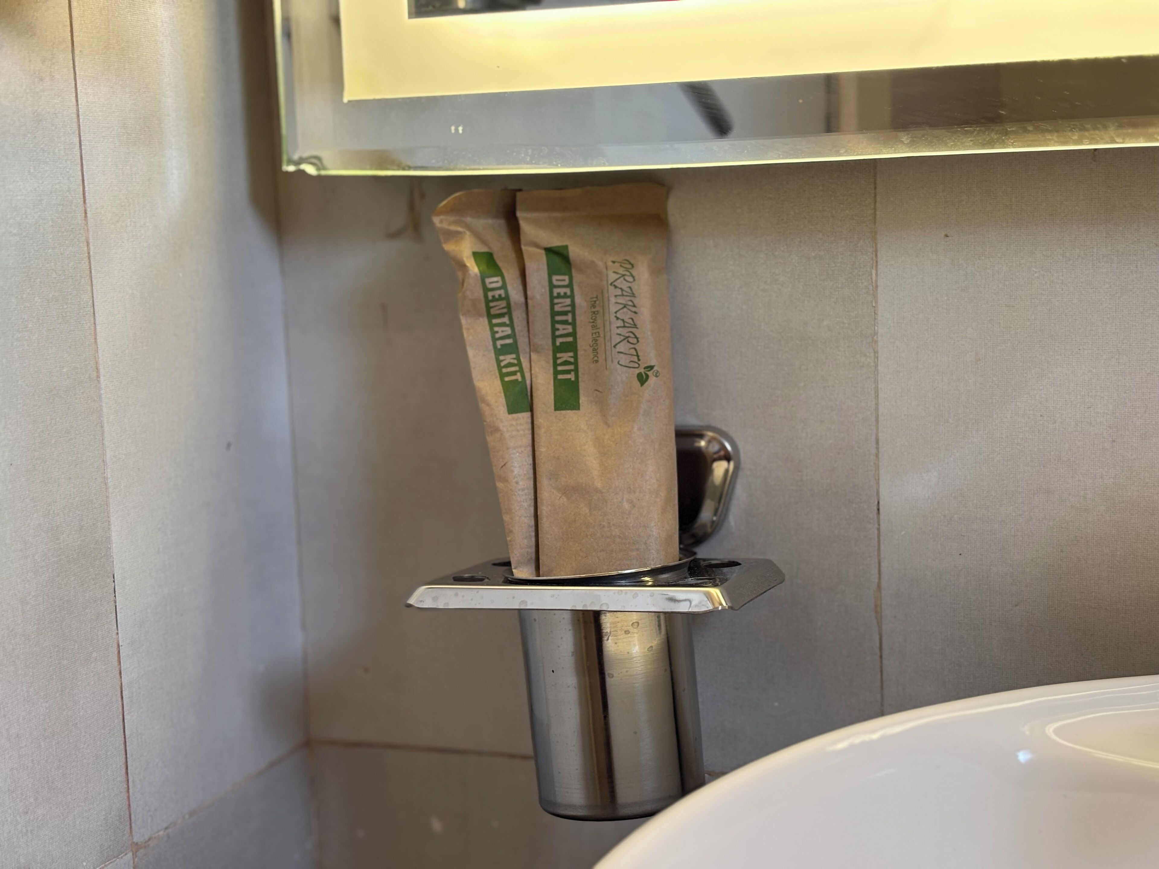 Un baño con un lavamanos blanco, un grifo de acero inoxidable y un dispensador de toallas de papel con etiqueta verde.