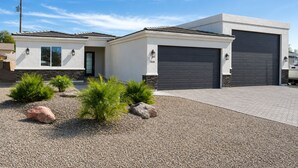 Een modern herenhuis met garage, oprit en beplanting van struiken en rotsen.