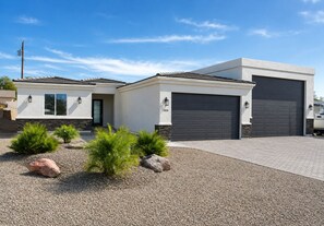 Ein modernes, zweistöckiges Haus mit Garage und Auffahrt, inmitten von Hecken und Steinen angelegt.