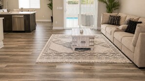 Een ruime woonkamer met een houten vloer, een salontafel, een bank en een plafondventilator.
