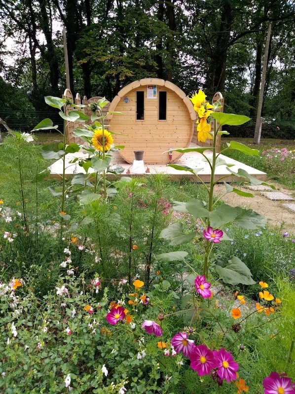 A wooden structure with a curved roof, surrounded by a garden with various flowers and greenery.