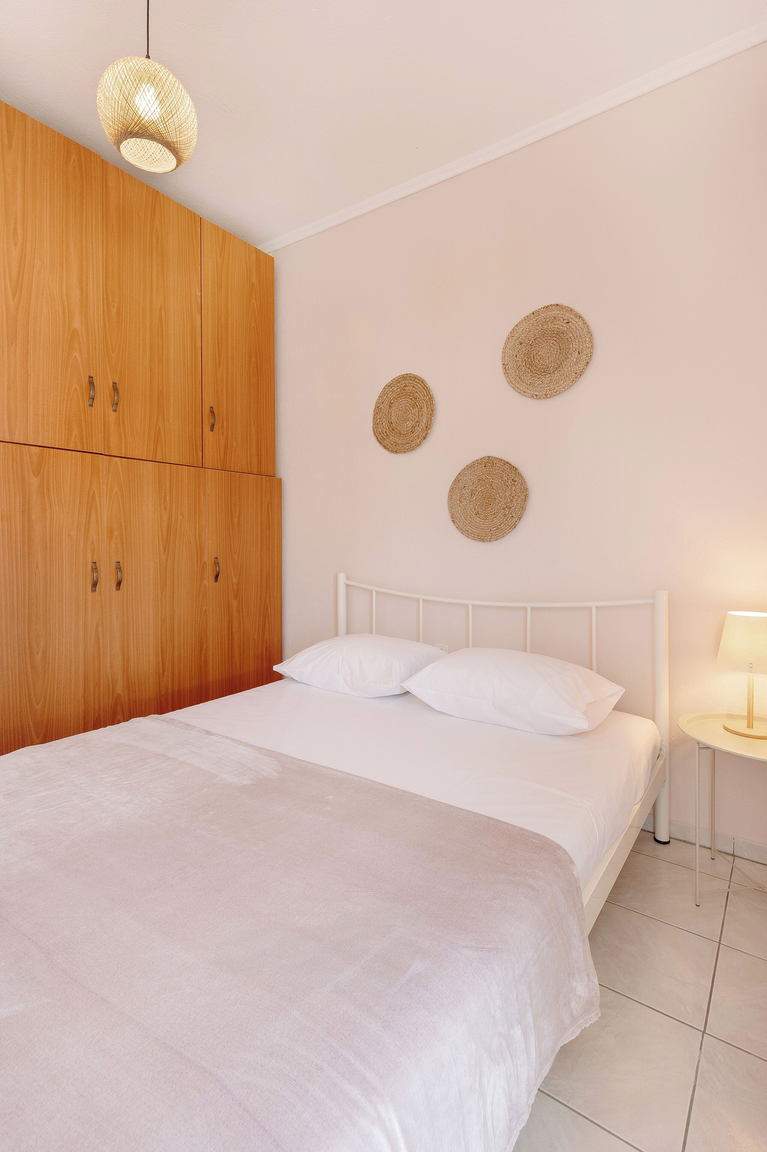 Un dormitorio con un armario de madera grande, una cama blanca con dos almohadas y una mesita de noche con una lámpara.