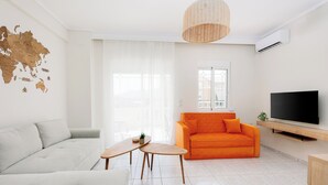 A modern living room with a white sofa, an orange sofa, a wooden coffee table, a flat-screen TV, and a world map on the wall.