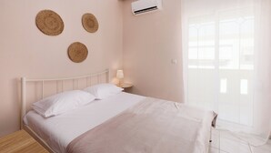 A bedroom with a bed, bedside table, lamp, air conditioning unit, and a window with curtains.