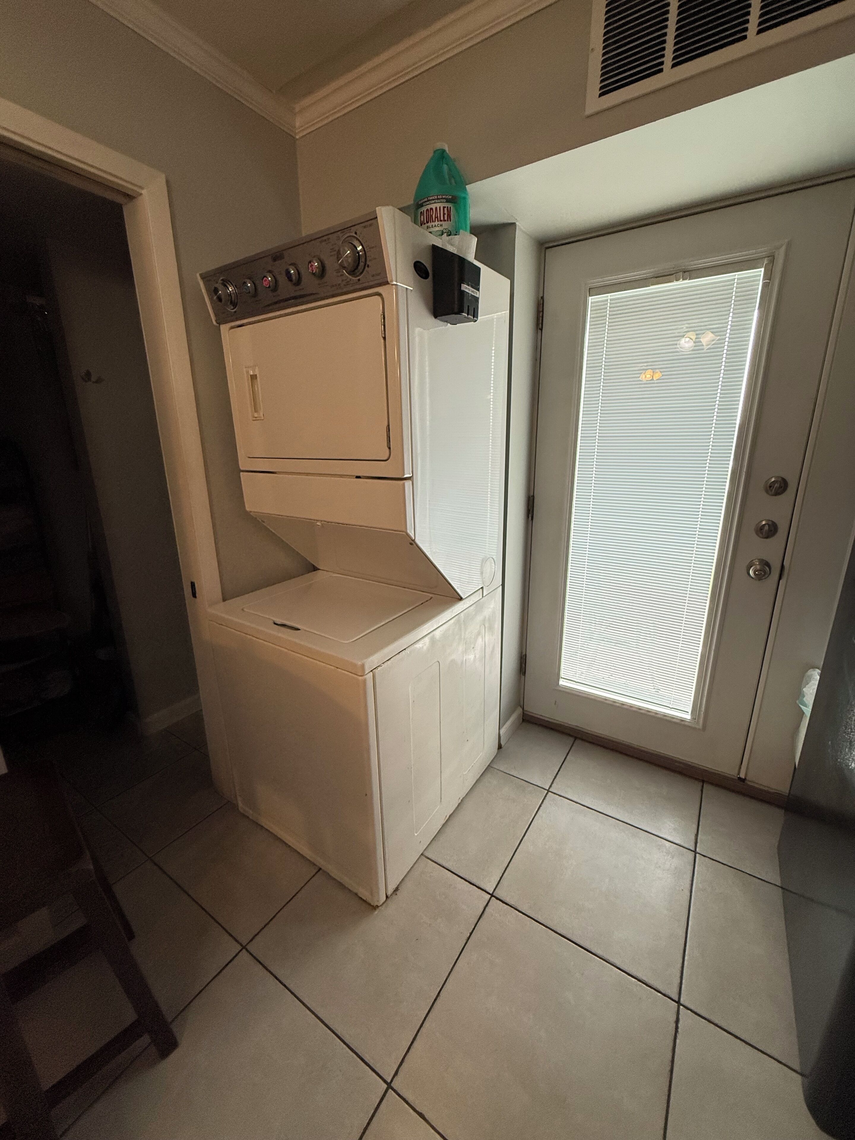 A compact laundry room with a washer and dryer, a door with a window, and a vent on the ceiling.