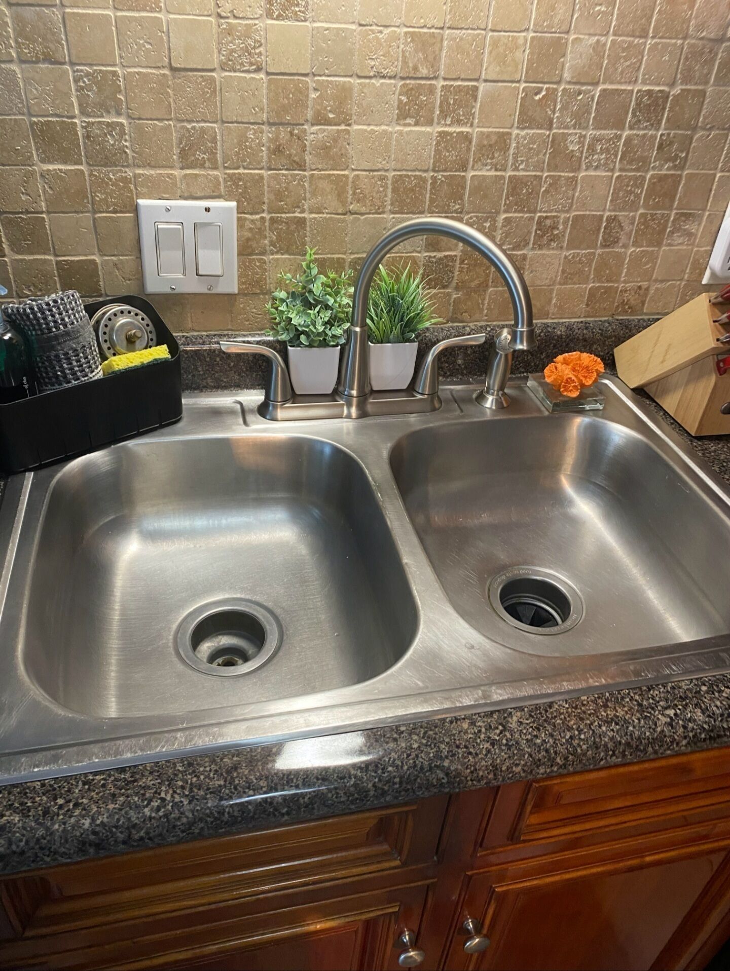 A kitchen with two stainless steel sinks, a granite countertop, wooden cabinets, a potted plant, and a knife block.