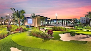 Un campo da golf con bunker di sabbia, un edificio con un grande schermo e palme.