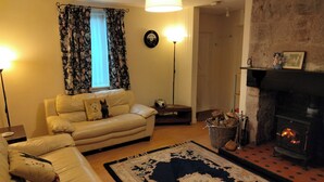 Een gezellige woonkamer met een bank, een vloerkleed, een open haard en een raam met gordijnen.