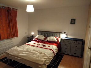 A bedroom with a bed, bedside tables, a lamp, a dresser, and a window with curtains.