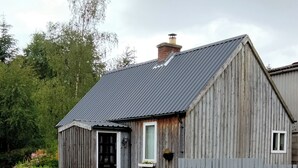 Een rustieke houten schuur met een metalen dak, een deur en een klein raam.