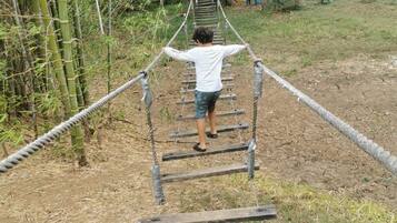 A child navigating a rope bridge in a natural setting with bamboo and trees.