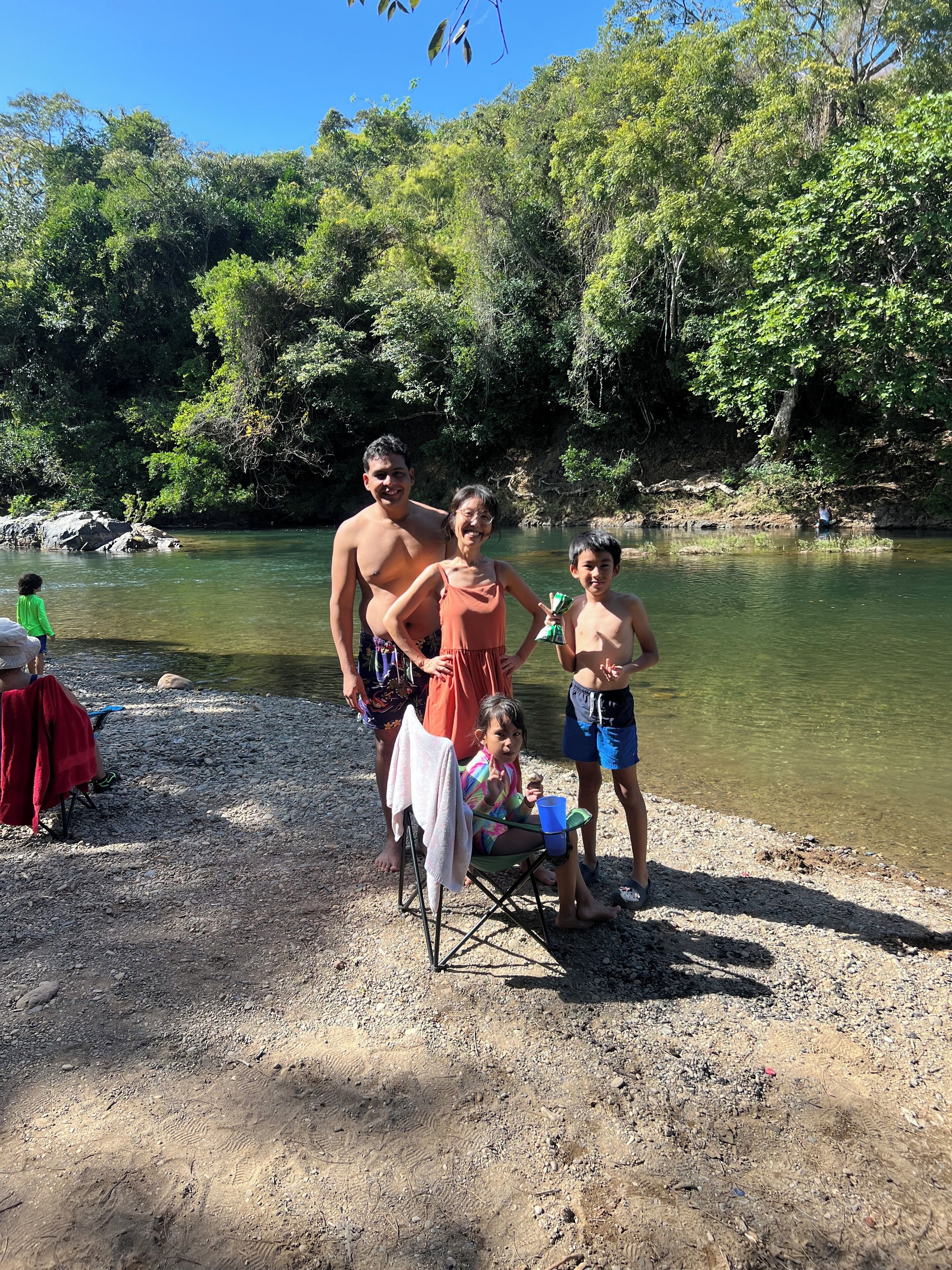 A group of people by a river with trees in the background.