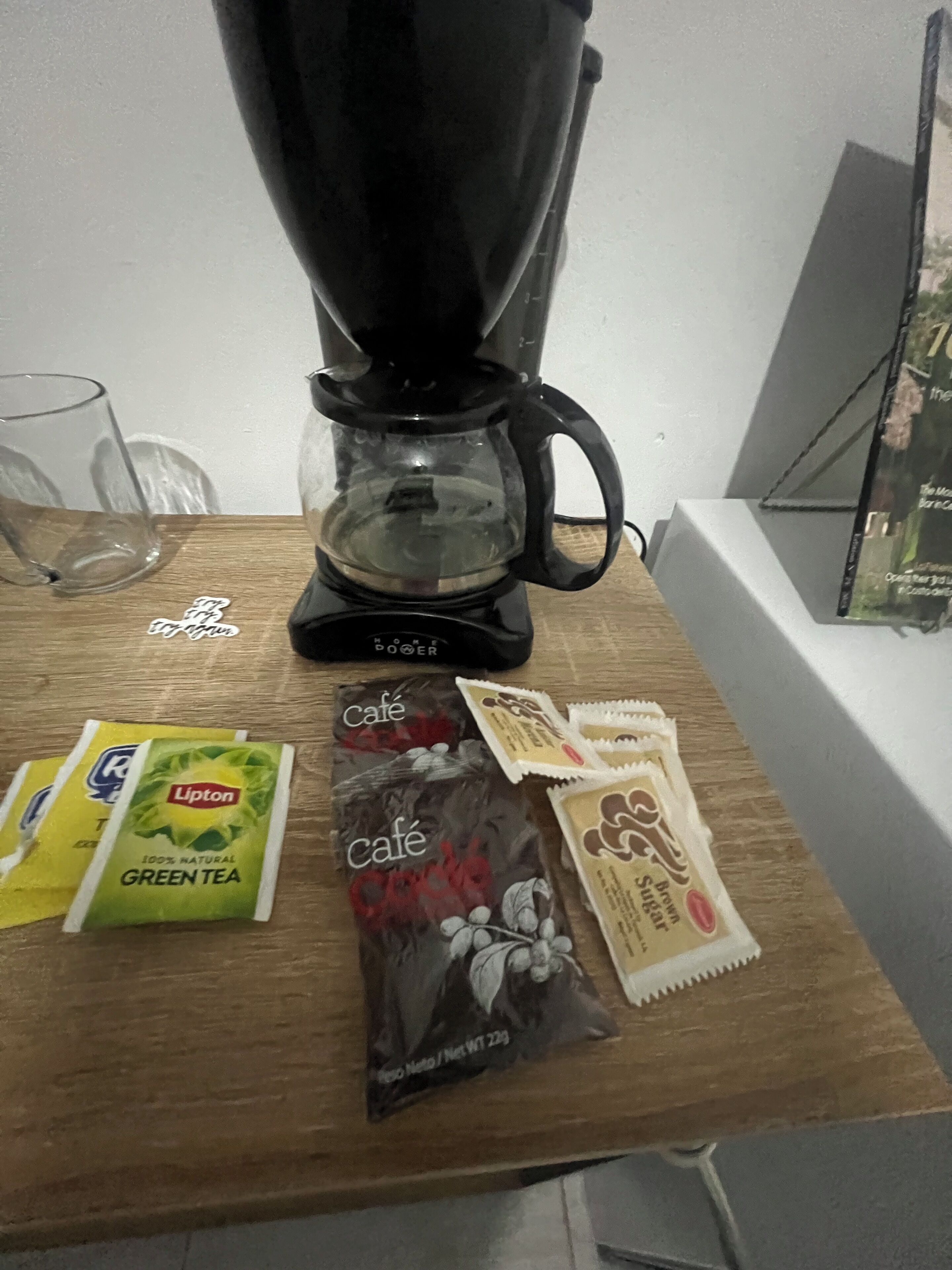 Une machine à café, des sachets de thé vert Lipton et des sachets de sucre pour le café, le tout posé sur une table en bois.