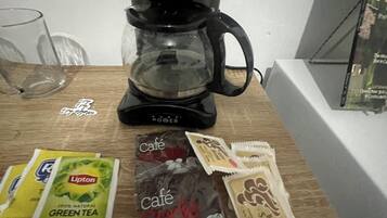 Une machine à café, des sachets de thé vert Lipton et des sachets de sucre pour le café, le tout posé sur une table en bois.