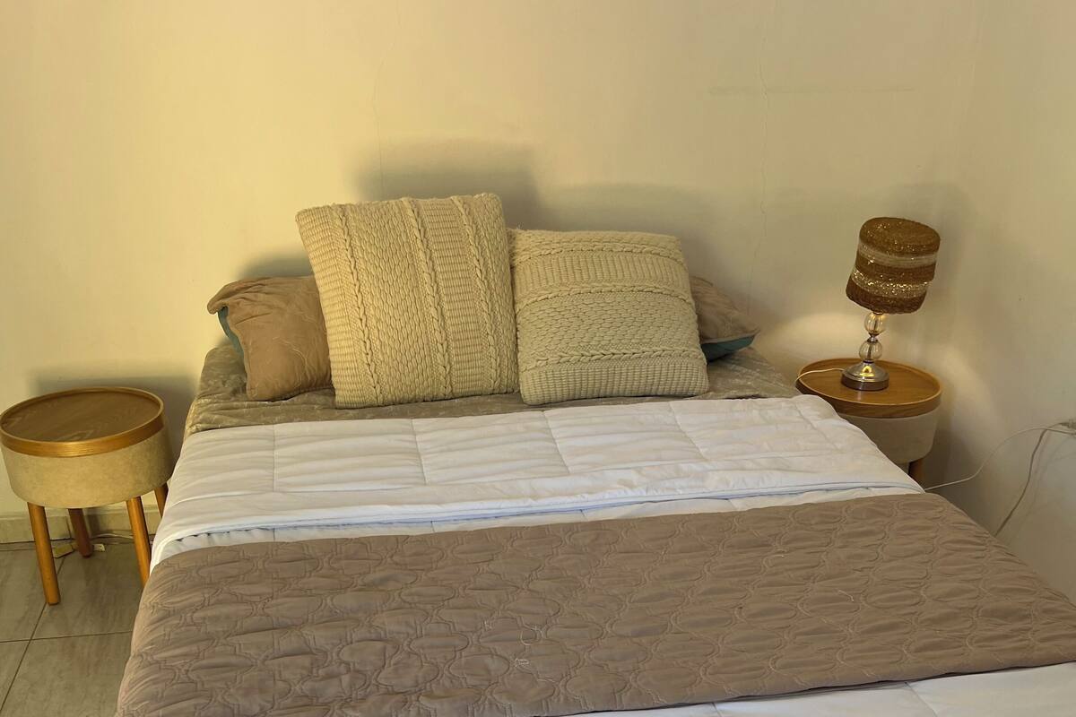 Ein Bett mit Decke, Kissen, einer Nachttischlampe und einem kleinen Holznachttisch.