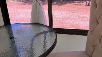Una habitación con una mesa de vidrio, una silla color crema y vistas a un espacio exterior con sillas y una pared.