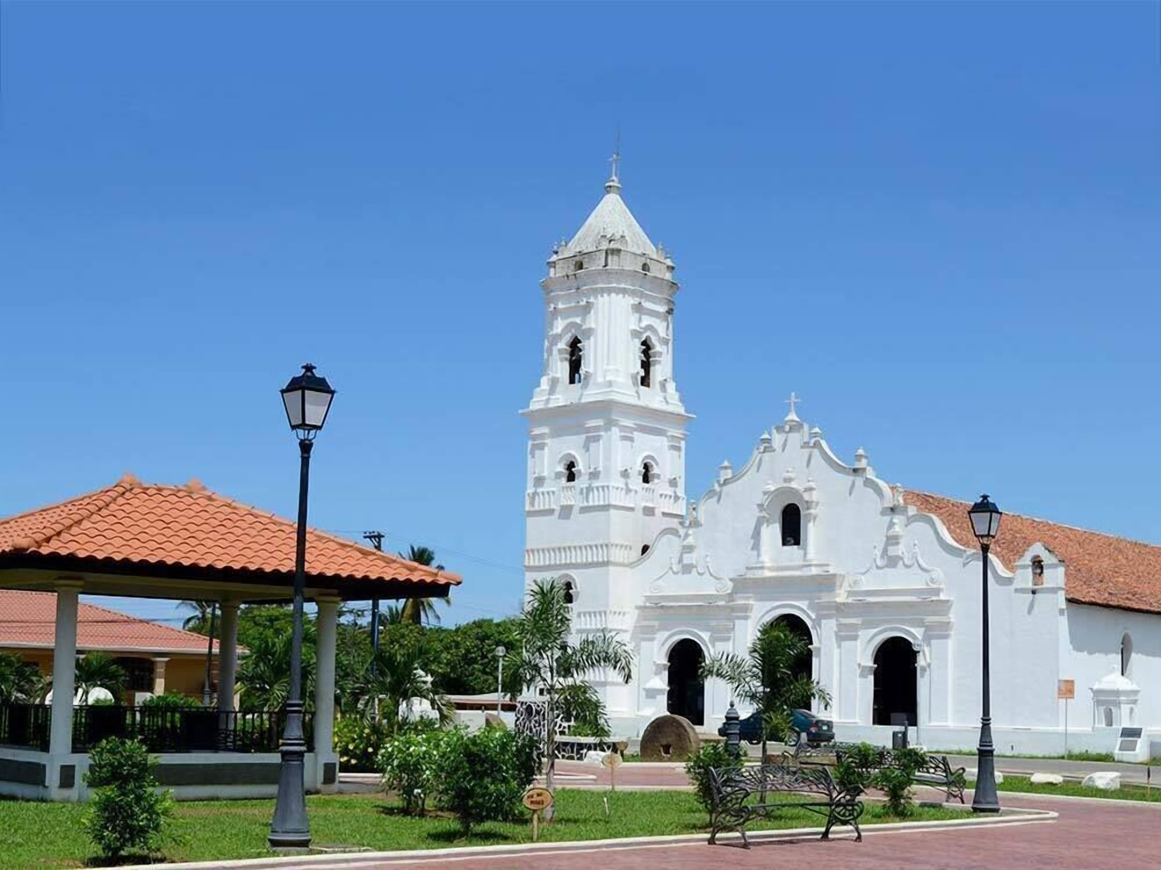 A white colonial-style building with a bell tower, a covered pavilion, and a park area with benches.