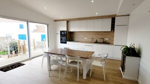 Une cuisine moderne avec des meubles blancs, un plan de travail en bois et un coin repas comprenant une table en bois et des chaises blanches.