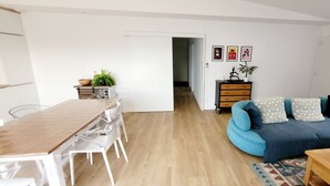 Un salon avec un canapé bleu, une table basse en bois et un coin repas comprenant une table et des chaises en bois.