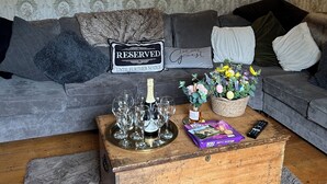 A living room with a grey sofa, a wooden coffee table with glasses and a bottle, and a mirror on the wall. - Beautiful 18th century 10 person Cottage in the heart of NE England w/hotub (Prudhoe)