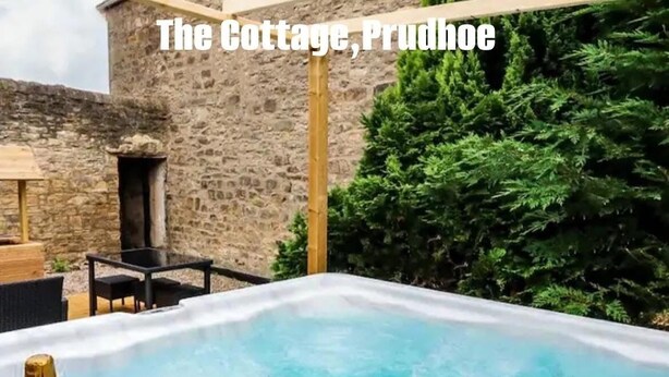 A hot tub with a bottle of champagne, surrounded by stone walls and greenery. - Beautiful 18th century 10 person Cottage in the heart of NE England w/hotub (Prudhoe)