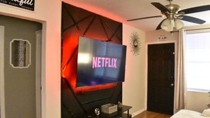 Ein Wohnzimmer mit einem an der Wand befestigten Fernseher, der das Netflix-Logo zeigt, einem Deckenventilator und einer Tür mit der Aufschrift "The Alamo".