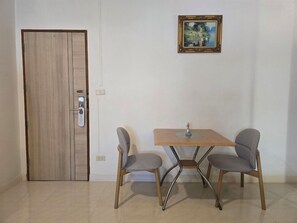 A room with a wooden door, a small table with two chairs, and a framed picture on the wall. - Smile Court Pattaya (Pattaya)