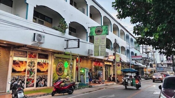 Vista de la calle con una fila de tiendas y un edificio de varios pisos con balcones.