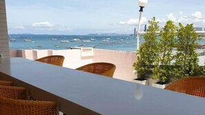 A balcony with wicker chairs, a white table, and a view of the sea with boats. - Smile Court Pattaya (Pattaya)