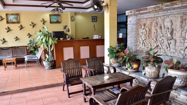 A reception area with a wooden reception desk, several wooden chairs, a large potted plant, and a stone wall with carvings. - Smile Court Pattaya (Pattaya)