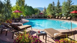 A pool area with lounge chairs and umbrellas, surrounded by trees and a mountain view.