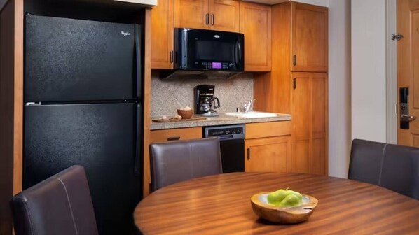 A compact kitchen with a refrigerator, microwave, coffee maker, and dishwasher. There is a wooden dining table with a bowl of fruit. - Sheraton Mountain Vista Villas 1-bedroom villa (Avon)