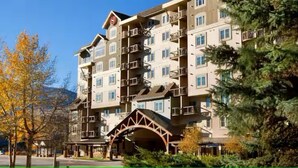 A multi-story hotel with balconies, a covered entrance, and a mountainous backdrop.